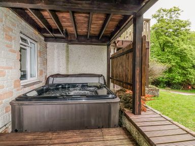 An outdoor hot tub under a wooden roof next to a stone wall at 23 Valley Lodge in Gunnislake
