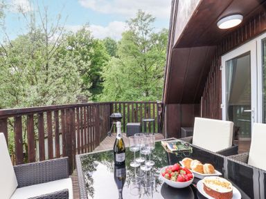 An outdoor balcony with a table set with strawberries cake and prosecco at 23 Valley Lodge in Gunnislake