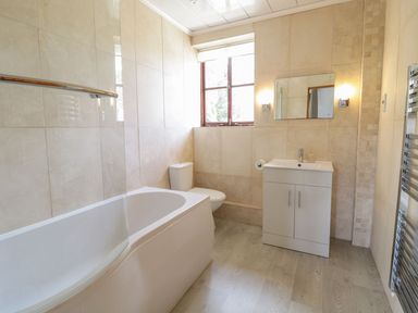A bathroom with a bathtub, toilet, sink, and mirror at Cyffdy Cottage - Arenig in Bala