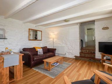 A living room with a leather sofa wooden coffee table and a television at Babes Cottage in Perranwell near Goonhavern