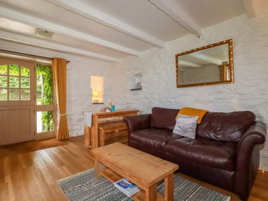A living room with a brown leather sofa a wooden coffee table and dining table and a door with yellow curtains at Babes Cottage in Perranwell near Goonhavern