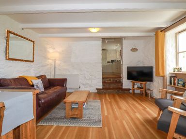 A living room with a brown leather sofa wooden coffee table flat screen tv and armchair at Babes Cottage in Perranwell near Goonhavern