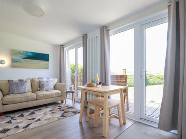 A living room with a beige sofa a wooden dining table and large glass doors at The Lookout in Perranwell near Goonhavern