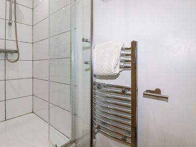 A shower area with white tiled walls and a chrome towel rack with a white towel at The Lookout in Perranwell near Goonhavern