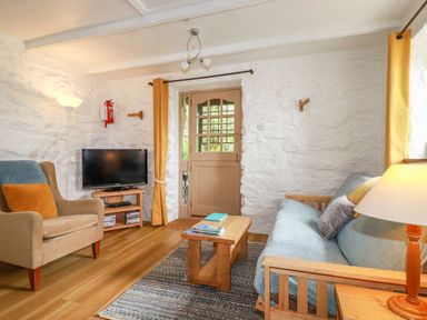 A living room with a sofa a chair a coffee table a wooden door and a television at Hollies Cottage Perranwell near Goonhavern