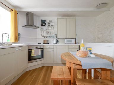 A kitchen with wooden floor cabinets a wooden table with bench seating and kitchen appliances at Hollies Cottage in Perranwell near Goonhavern