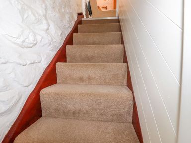 A carpeted staircase with white textured wall on the left and white paneled wall on the right at Hollies Cottage in Perranwell near Goonhavern