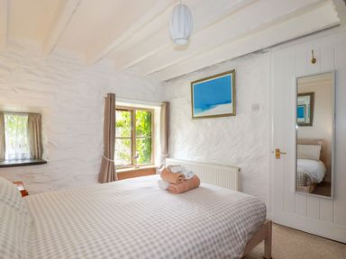 A bedroom with a bed covered in checked bedding and towels on top a window with curtains and a framed picture on the wall at Hollies Cottage in Perranwell near Goonhavern