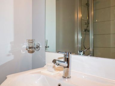 A bathroom sink with a chrome faucet a soap dish with a bar of soap a glass holder and a mirror with a shower visible in reflection at Hollies Cottage in Perranwell near Goonhavern
