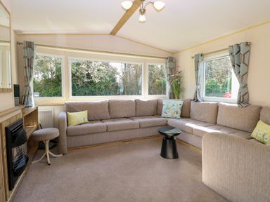 A living room with a large beige sectional sofa and small black round table at 4 Foxburrow Hang in Fritton near Belton Norfolk