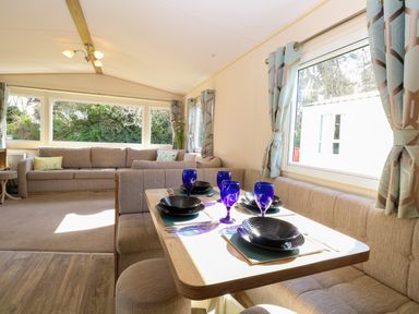 A dining area with a table set with blue glasses and black plates beside a window with patterned curtains and a living room with a beige sofa at 4 Foxburrow Hang in Fritton near Belton Norfolk