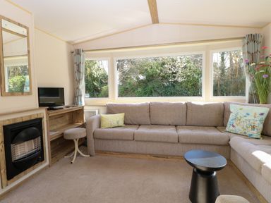 A living room with a beige sectional sofa pillows small table fireplace and large windows showing trees at 4 Foxburrow Hang in Fritton near Belton Norfolk