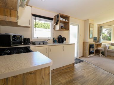 A kitchen with countertop appliances and sink next to a living area with fireplace and window at 4 Foxburrow Hang in Fritton near Belton Norfolk