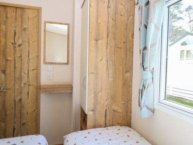 A bedroom corner with two single beds wooden door wooden-framed mirror small wooden shelf and window with light blue patterned curtains at 4 Foxburrow Hang in Fritton near Belton Norfolk