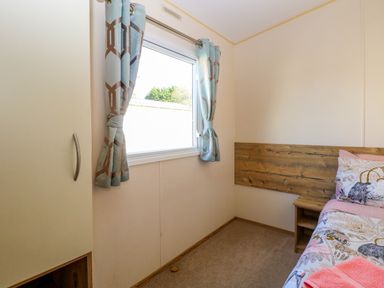 A bedroom with a window with curtains a wardrobe and a bed with a wooden headboard at 4 Foxburrow Hang in Fritton near Belton Norfolk