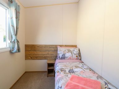 A small bedroom with a single bed a wooden headboard a nightstand and a window with curtains at 4 Foxburrow Hang in Fritton near Belton Norfolk