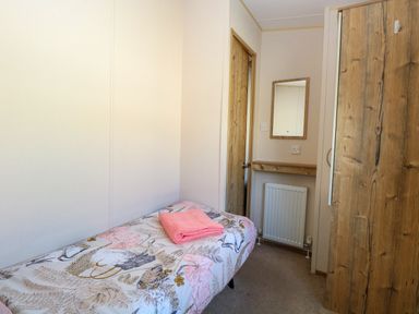 A small bedroom with a single bed with patterned bedding a pink towel a wall mirror a radiator and a wooden wardrobe at 4 Foxburrow Hang in Fritton near Belton Norfolk