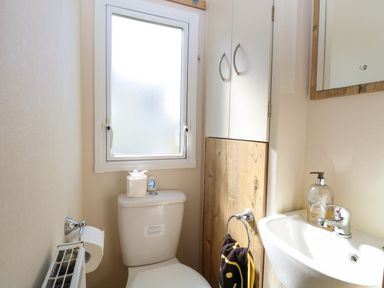 A small bathroom with a toilet under a frosted window a wall-mounted cabinet a sink with hand soap and a towel at 4 Foxburrow Hang in Fritton near Belton Norfolk