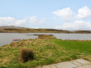 A view of a grassy area leading to a body of water with a small boat and hills in the background at Erraid in South Cuan near Cullipool Isle Of Luing