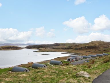 A row of pod-shaped cabins near a body of water with hills in the background at Erraid South Cuan near Cullipool Isle Of Luing