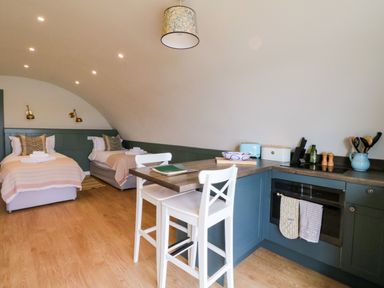A room with two single beds and a kitchen area with a breakfast bar and two white stools at Insh Cullipool Isle Of Luing