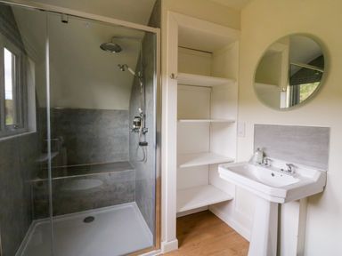 A bathroom with a shower enclosure a pedestal sink a round mirror and built-in shelving at Insh Cullipool Isle Of Luing