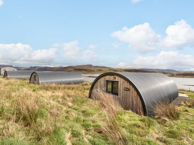 Three curved metal and wood cabins on grassy land near a body of water at Insh Cullipool Isle Of Luing