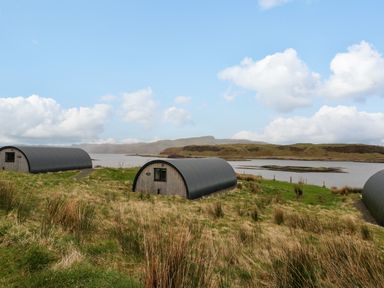 Three small curved-roof cabins on grassy land near a body of water with hills in the background at Insh Cullipool Isle Of Luing