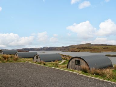 Curved roof cabins near a body of water with hills in the background at Insh Cullipool Isle Of Luing