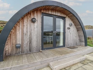 A wooden curved front entrance with glass double doors and steps at Sula in Cullipool Isle Of Luing