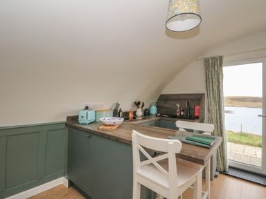 A kitchen with blue cabinets a wooden countertop a white chair a toaster and a door with a view at Sula Cullipool Isle Of Luing