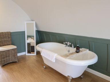 A bathroom with a freestanding bathtub a wicker chair and a floor mirror at Sula in Cullipool Isle Of Luing