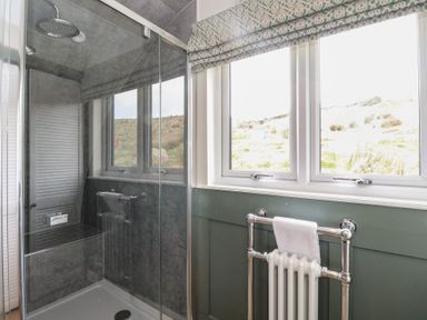 A bathroom with a glass shower enclosure a window with patterned blinds and a wall-mounted towel radiator at Sula in Cullipool Isle Of Luing