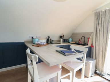 A small kitchen area with a breakfast bar two white chairs and kitchen appliances at Scarba in Cullipool Isle Of Luing