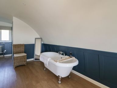 A bathroom with a freestanding bathtub a wicker chair and a floor mirror at Scarba in Cullipool Isle Of Luing