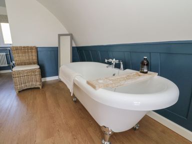 A bathroom with a white clawfoot bathtub a wicker chair and a floor mirror at Scarba in Cullipool Isle Of Luing