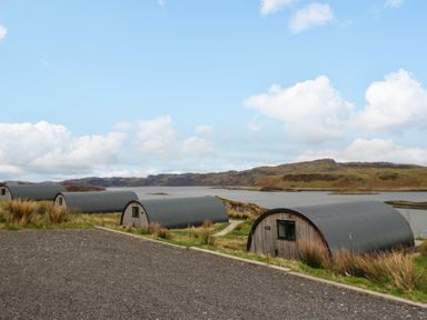 Four curved wooden cabins with black roofs near a body of water and hills in the background at Torsa Cullipool Isle Of Luing