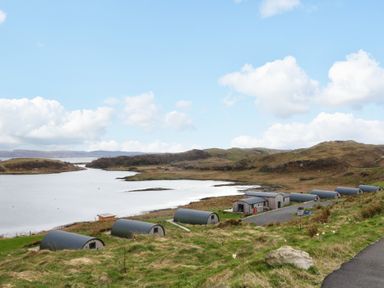 A row of small cabins near a body of water with hills in the background at Torsa Cullipool Isle Of Luing