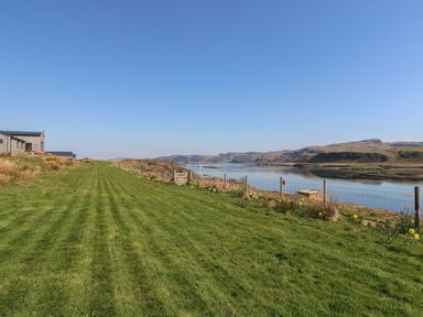 A grassy yard with a wooden fence and gate overlooking a body of water and hills at Torsa Cullipool Isle Of Luing