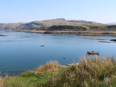 A body of water with two boats and grass in the foreground at Torsa Cullipool Isle Of Luing