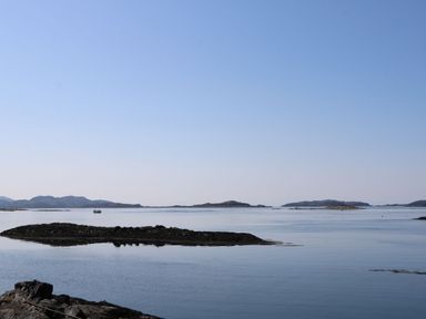 A calm coastal scene with small rocky islands and a boat in the water at Torsa in Cullipool Isle Of Luing