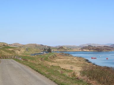 A road leading to green hills by a body of water with boats at Torsa Cullipool Isle Of Luing