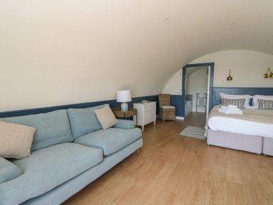 A bedroom with a blue sofa white nightstand bed and wooden floor at Torsa Cullipool Isle Of Luing
