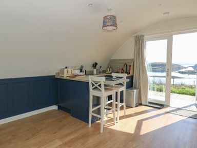 A kitchen corner with blue cabinets a small countertop table with two white chairs and glass doors overlooking a water view at Torsa in Cullipool Isle Of Luing