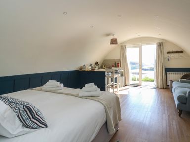 A bedroom with a bed a kitchenette a sofa and glass doors leading outside at Torsa in Cullipool Isle Of Luing