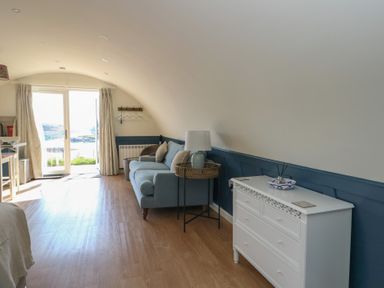 A room with a blue sofa a white chest of drawers a side table and a door with curtains leading outside at Torsa in Cullipool Isle Of Luing