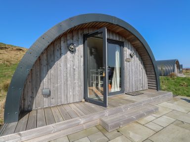 A wooden curved cabin with glass door open and steps leading to a paved patio at Torsa in Cullipool Isle Of Luing