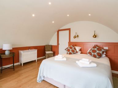 A bedroom with a double bed two patterned pillows white towels wicker chair white dresser and side table with lamp at Losal Cullipool Isle Of Luing