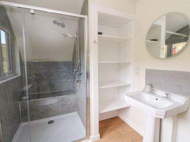 A bathroom with a glass shower enclosure open white shelves and a white pedestal sink with a round mirror at Losal Cullipool Isle Of Luing