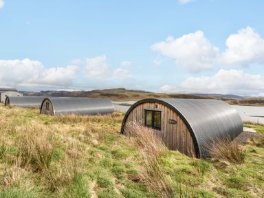 A group of curved metal and wooden cabins on grassy land near water at Losal Cullipool Isle Of Luing